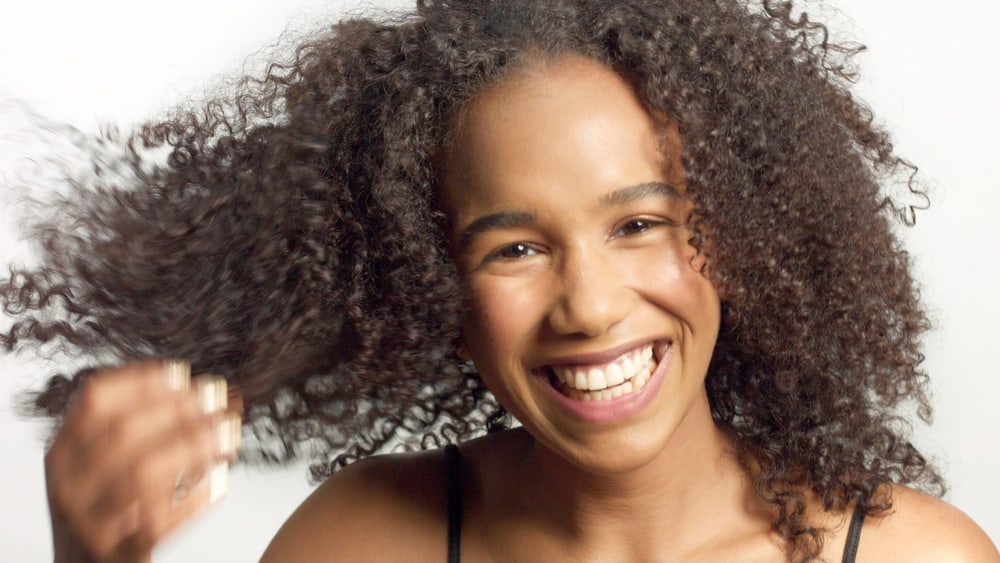 Beautiful black woman wearing make-up with type 3 natural hair while looking at the camera laughing. 