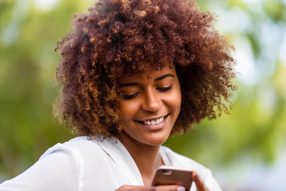 Pretty black girls with natural hair reading an article on her mobile phone while sitting on a bench at the park