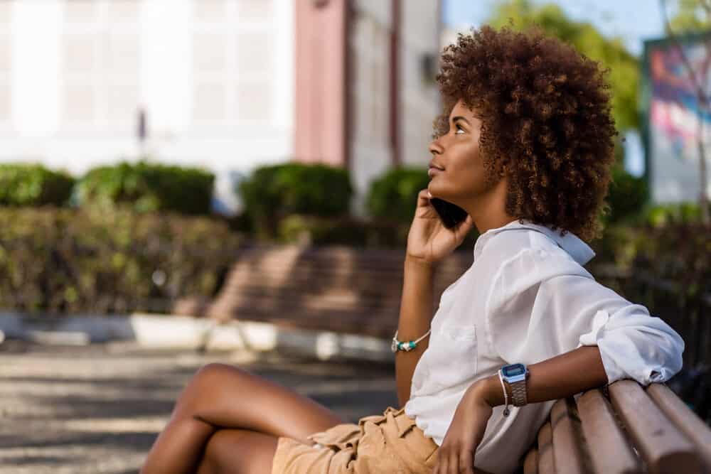 American female wearing a white dress shirt and brown shorts with brassiness in her light brown curly hair strands