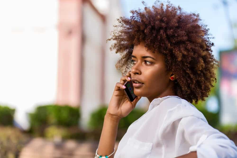 Cute black girl with a short curly haircut talking on the mobile phone in the park