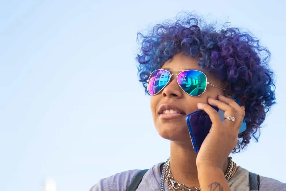 How to Dye Dark Hair Purple With and Without Bleach at Home 7 Mixed-race Latin black girl outside talking on a mobile phone with curly hair strands.