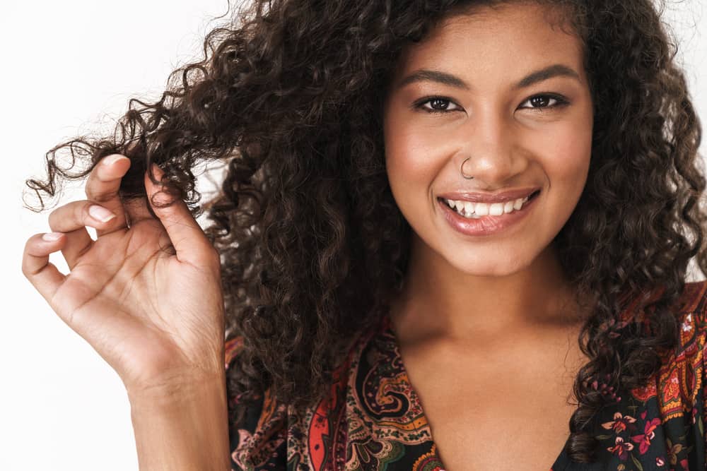 Black woman with wavy hair and a nose ring biting her lip, while wearing a multi-colored dress.