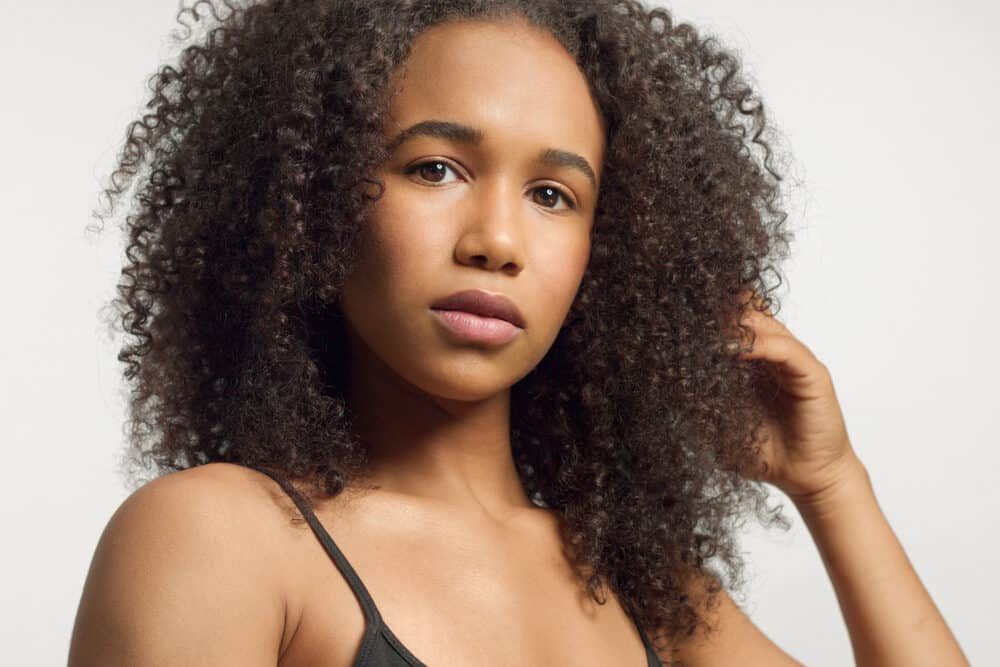 A woman with one hand in her curls, looking at the camera