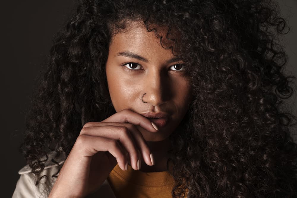 Beautiful African American female with a nose ring and type 3 naturally curly hair holding her lip.