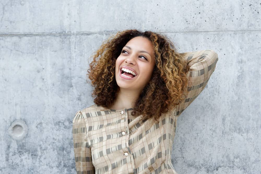 Black women relaxing against a wall with her left arm behind her head