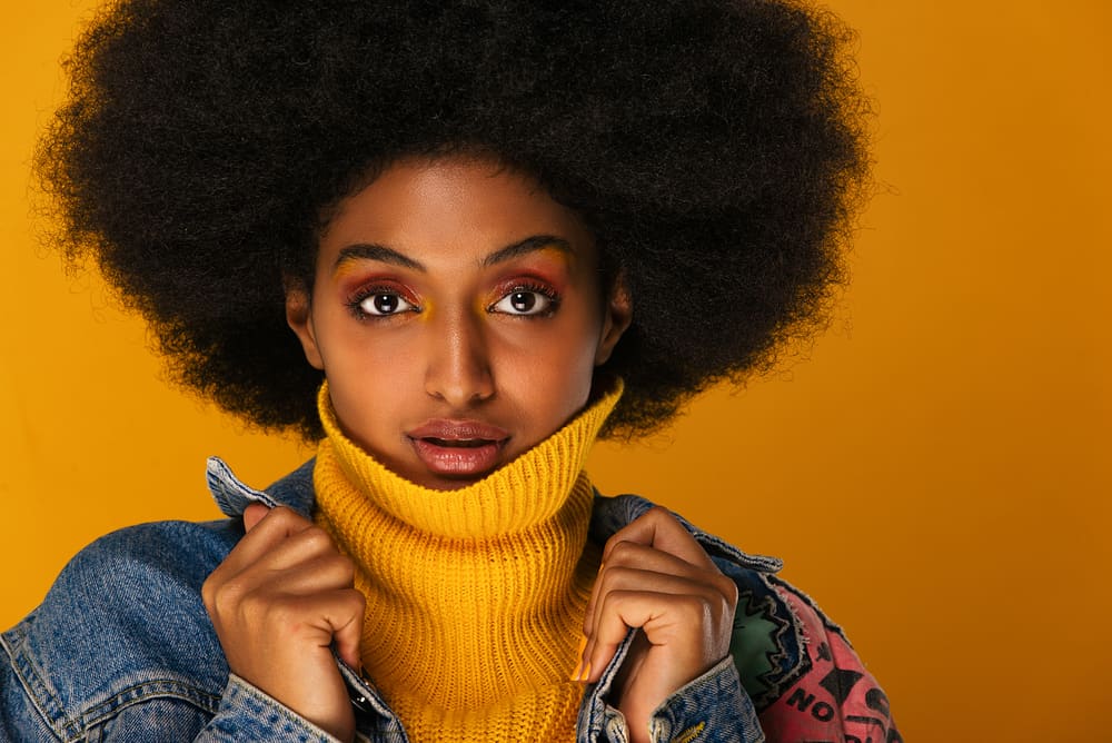 Light-skinned female with 4c natural curls wearing a blue jean jacket and yellow sweater