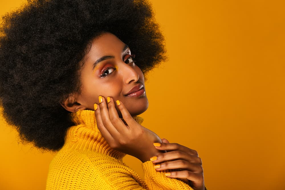 Young black female wearing a yellow sweater and fingernails with naturally curly hair with a fresh henna mixture