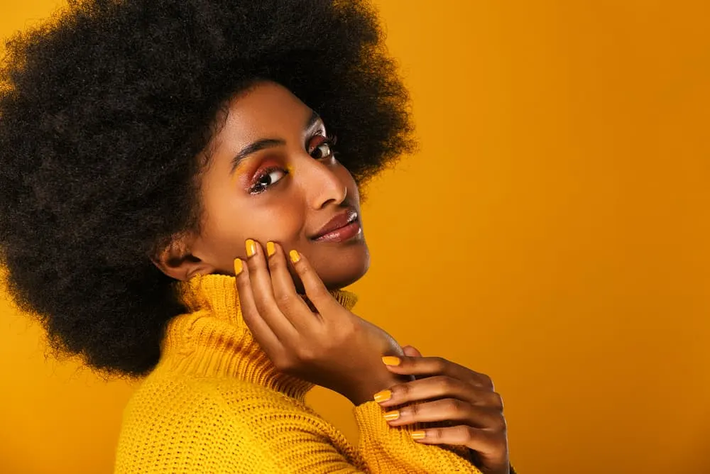 Young black female wearing a yellow sweater and fingernails with naturally curly hair with a fresh henna mixture
