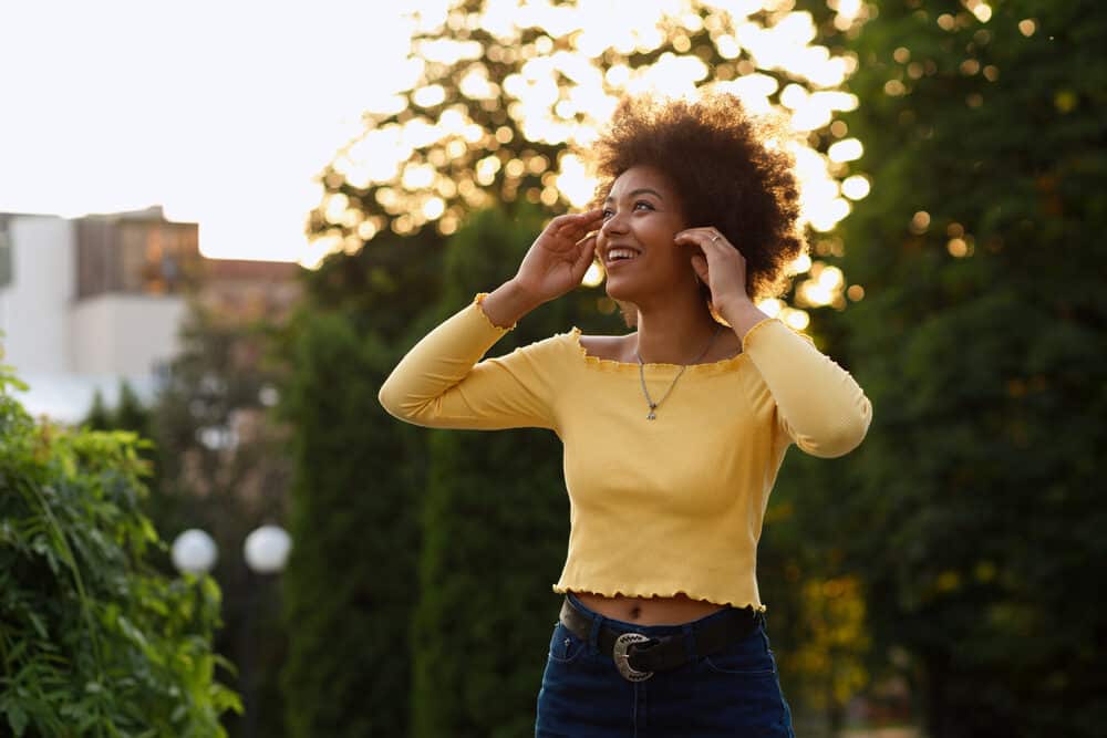 African American girl in the park running her fingers through her own hair strands while looking up into the sky