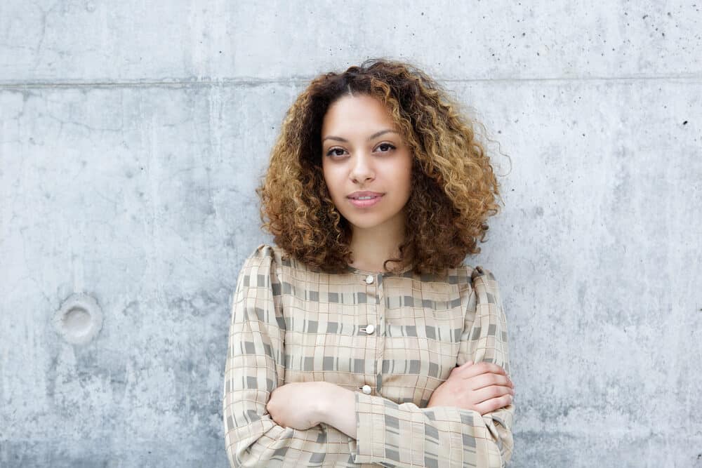 Cute black female standing outside with her arms crossed wearing a brown and green dress shirt