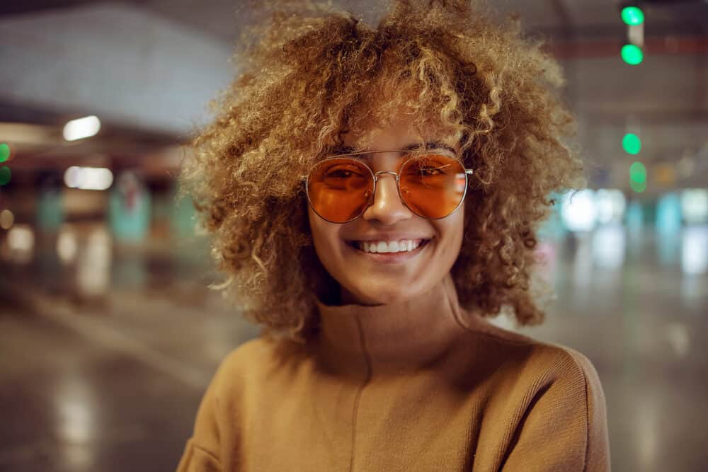 A striking smile is plastered across this young woman's face as she gazes confidently into the camera. You can see her beautiful, dark skin and a strand of hair cascading over one eye in all its glory.