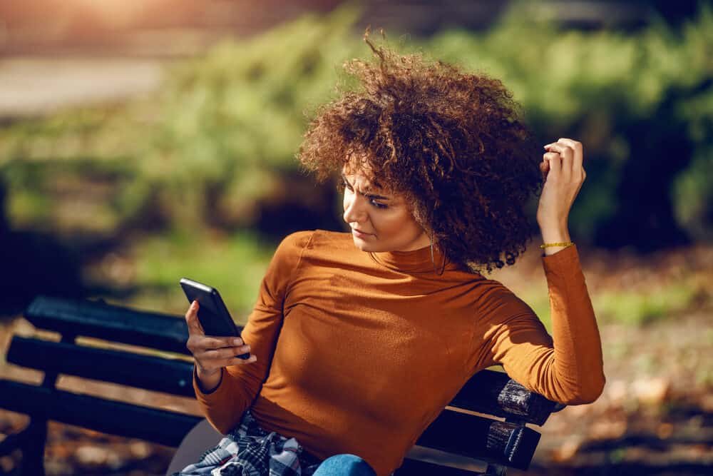 A young woman with a mixed-race in New York City is sitting on a bench using her phone.