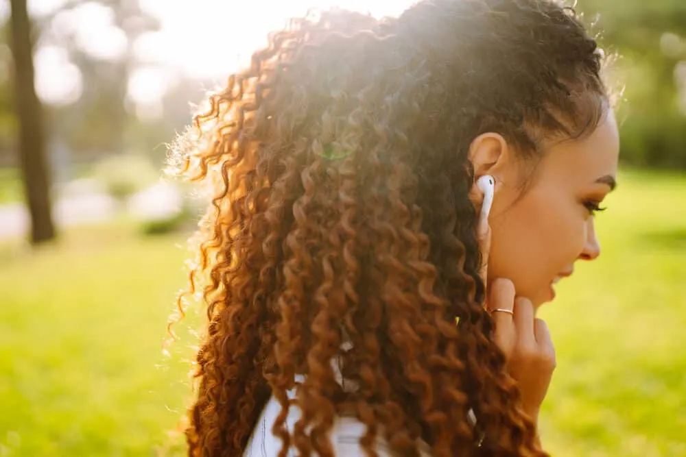 Can You Put Lotion in Your Hair? What Happens? Definitive How to Guide 1 African American girl with curly hair follicles wearing Apple air pods