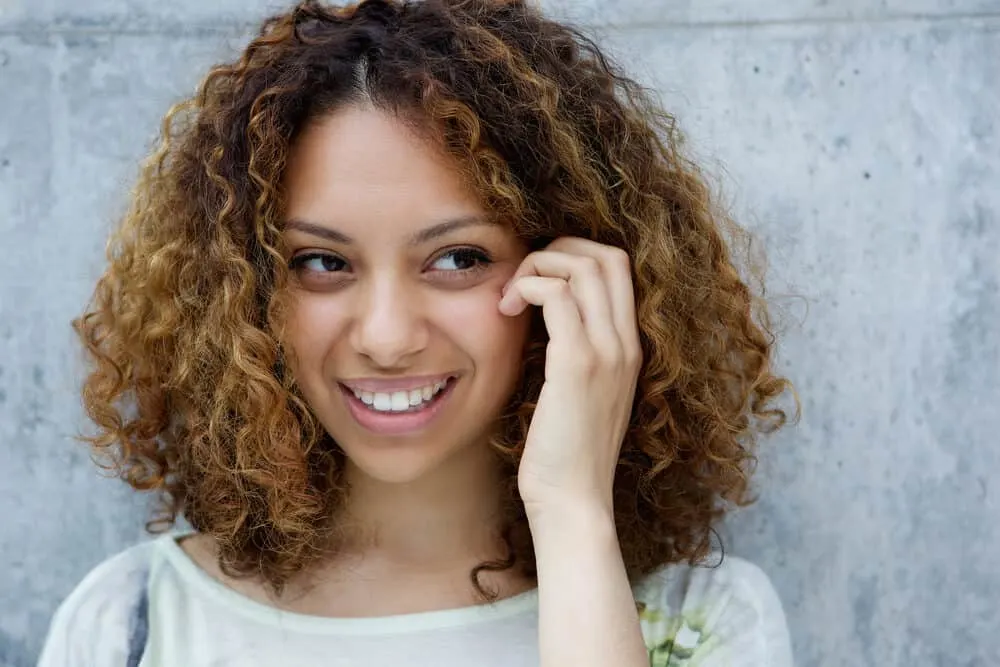 Learn How to Use Coconut Oil Before Bleaching Hair: Step-by-Step Guide 1 Light-skinned black girl with curly bleached hair wearing a big smile while touching her face