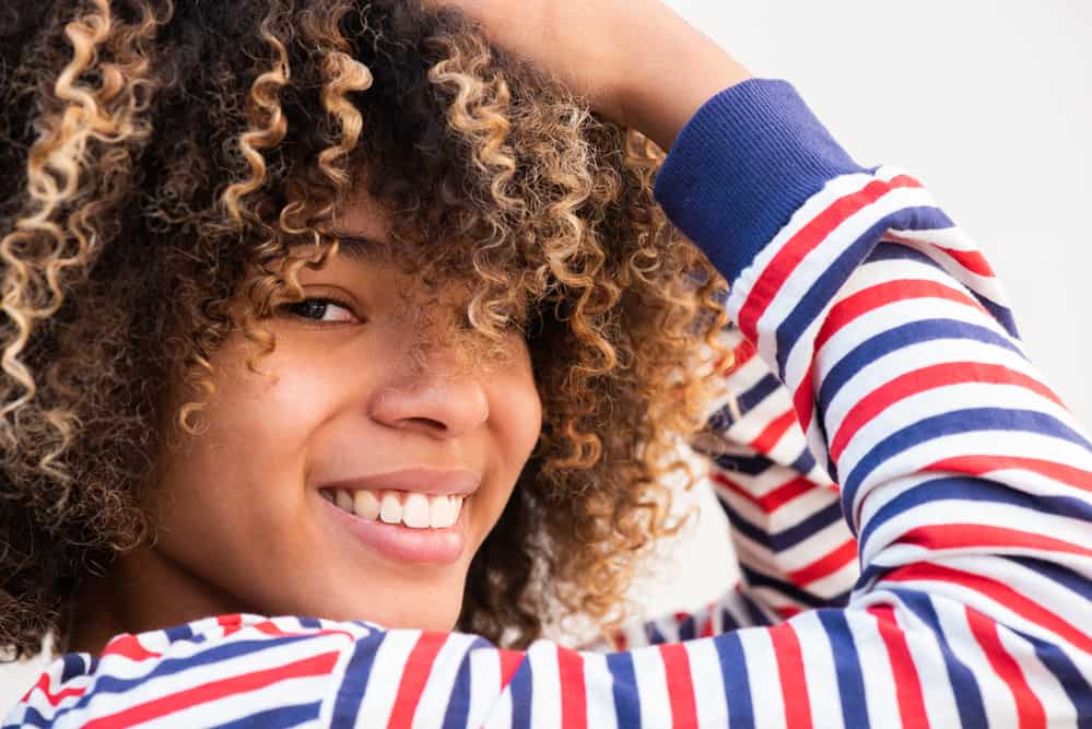 Close-up of black female wearing curly hair and a red and blue shirt looking directly into the camera.