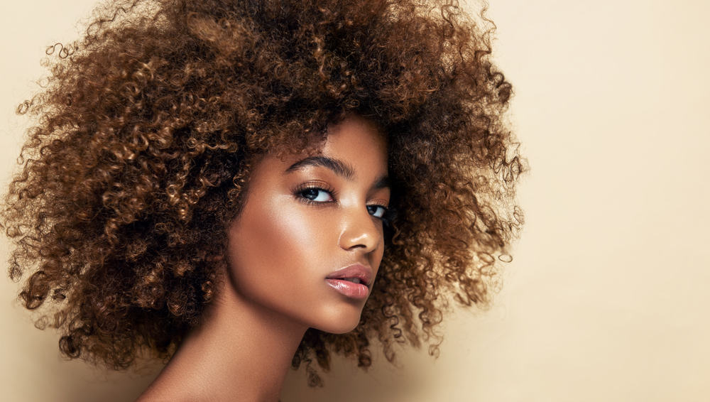 Cute black female with brown curls, freshly arched eyebrows, and pink lipstick.