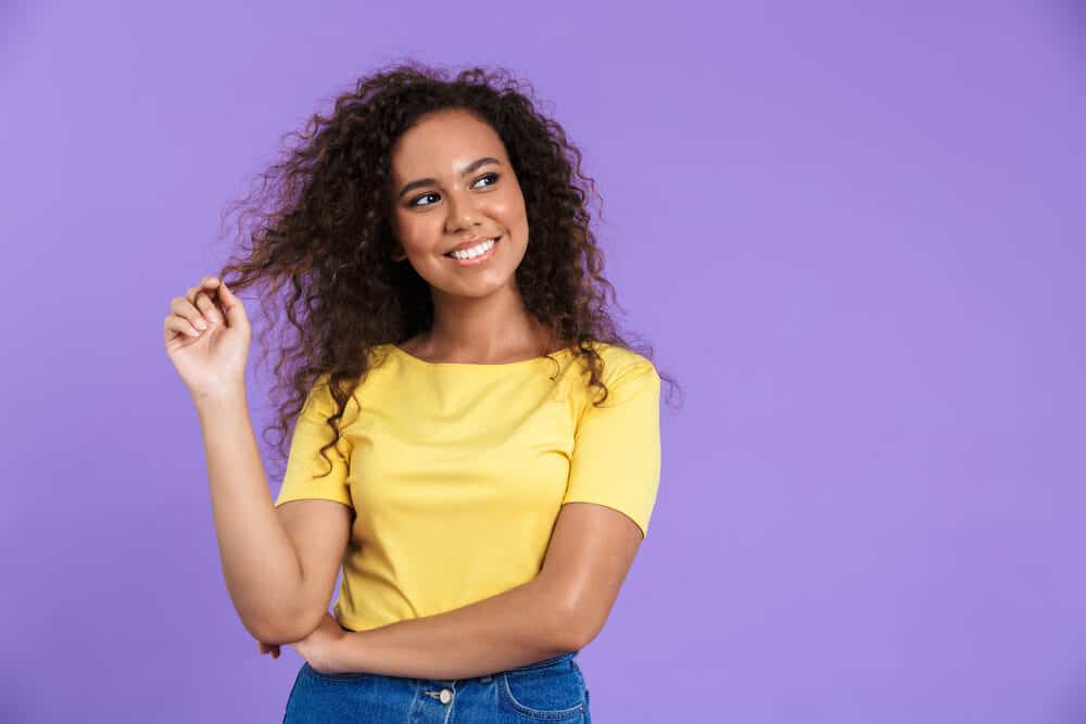 A cute mixed-race woman with naturally curly hair wearing a yellow t-shirt and blue jeans