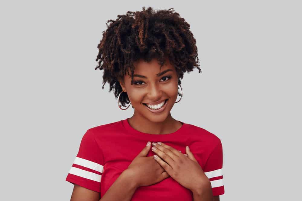 Black girl wondering how to detangle matted hair while wearing a red shirt with white stripes on the sleeves