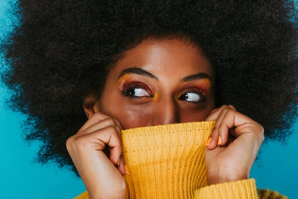 Dark skinned female hiding her face behind a yellow sweater with a 4c hair type