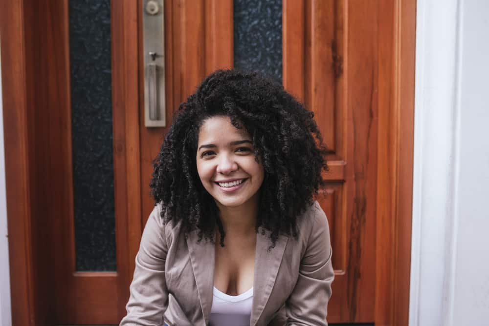 Mexican female sitting on steps outside after getting off work wearing a brown jacket and white undershirt