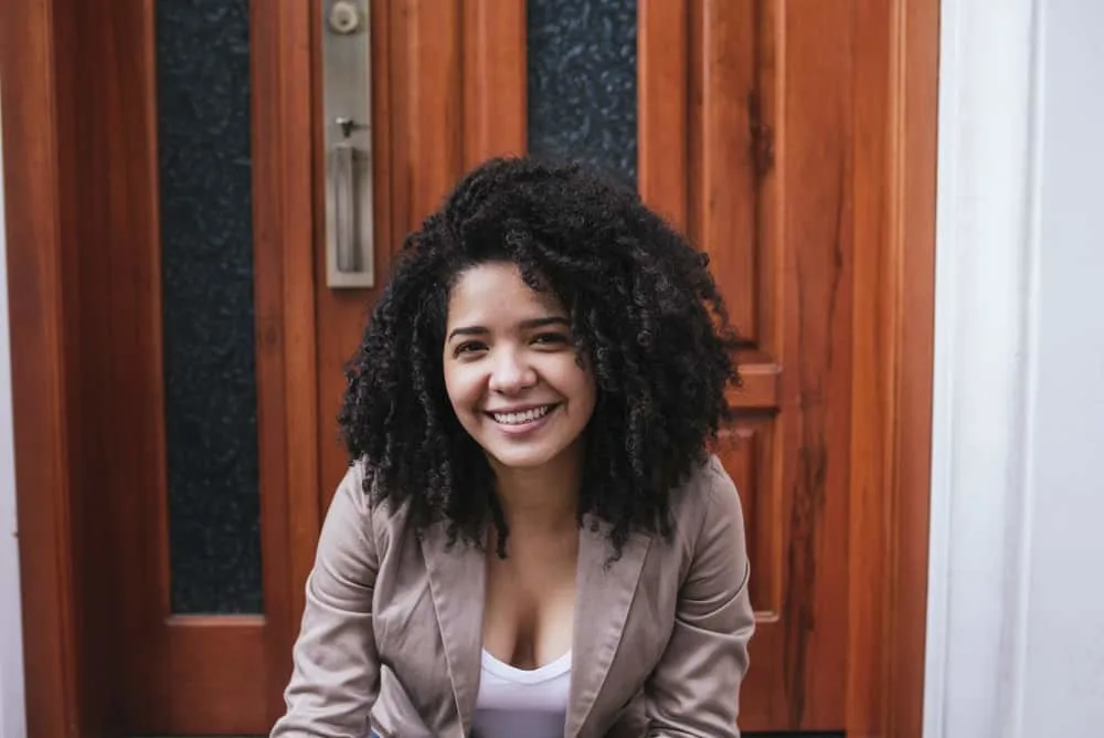 Using Chile Shampoo for Hair Growth: Learn How and Why It Works 4 Mexican female sitting on steps outside after getting off work wearing a brown jacket and white undershirt