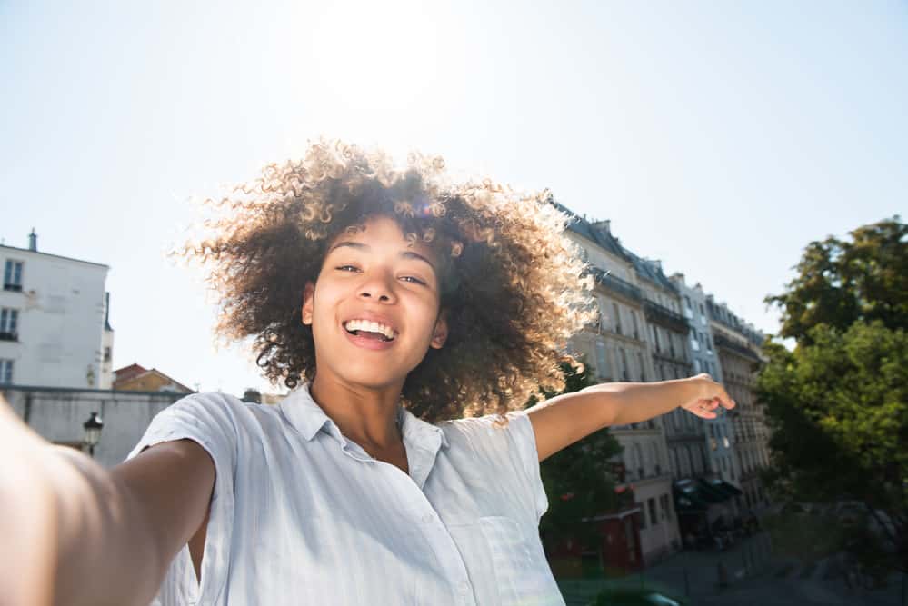 Cute black women with type 3c curls outside taking a selfie with her iPhone 12 in the park.