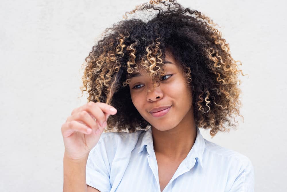 Black female playing with the natural oils in her hair after using Dove's shampoo and conditioner.