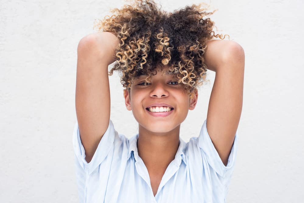 Hispanic women holding her hair in a pineapple style wearing a casual blue button-down shirt.