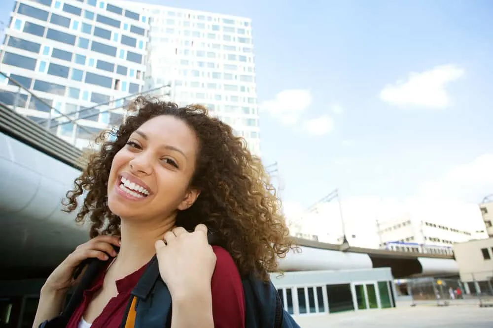 Smiling lady with natural hair standing outside wearing a backpack on a sunny day