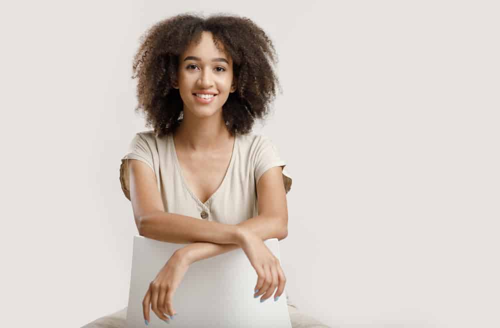 Young African American blogger with naturally curly hair sitting on a white chair