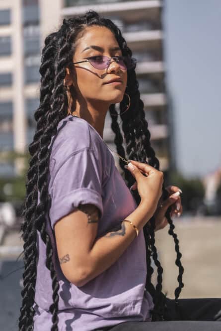 Light skinned female sitting on a park bench in South America wearing a long braided hairstyle with white fingernail polish