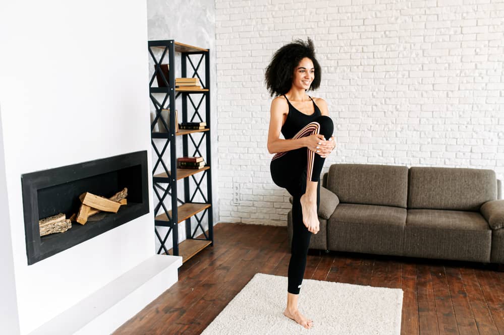 An African-American girl with 4b natural hair in sportswear is stretching her legs in a cozy living room.