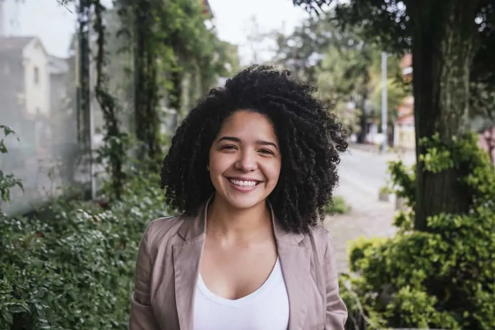 Using Chile Shampoo for Hair Growth: Learn How and Why It Works 2 Cute Mexican lady with amazing 3c natural curls and black eyes wearing a white shirt, brown jacket, and pink lipstick
