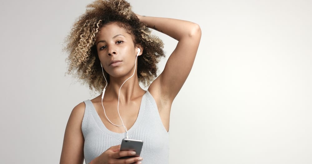 A black woman with blonde curly hair and freckles, wearing a gray tank top and pink lipstick