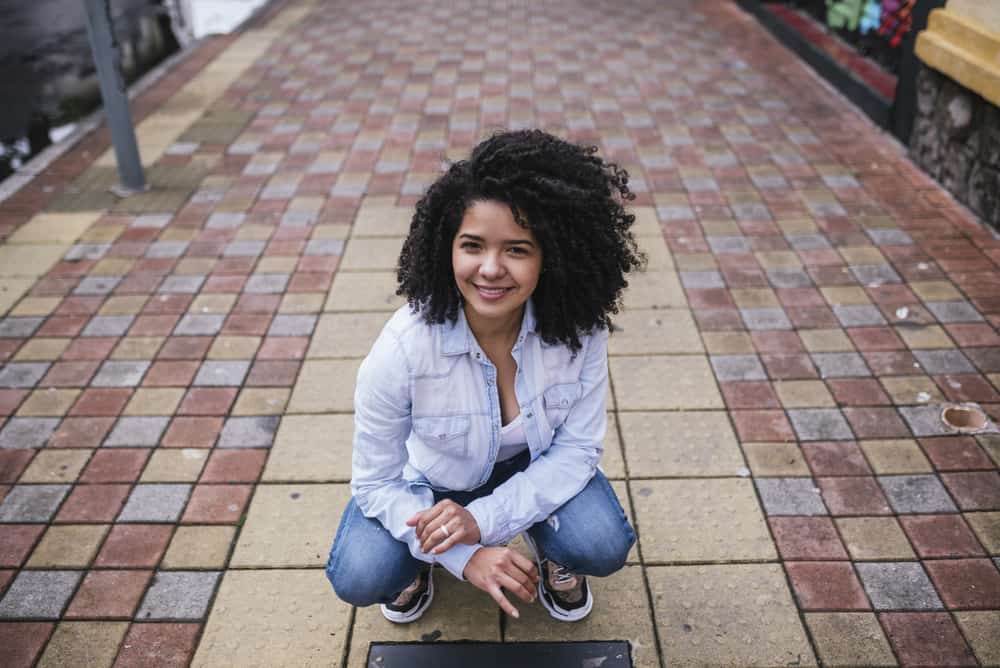 Hispanic woman wearing a light blue denim dress shirt and blue jeans with sneakers