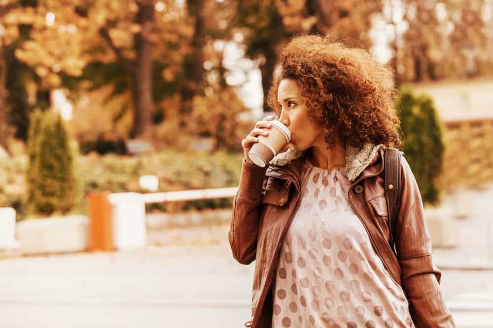 kiharatukkainen nainen seisoo ulkona juomassa kahvia kävellen Alabaman Birminghamin keskustassa.