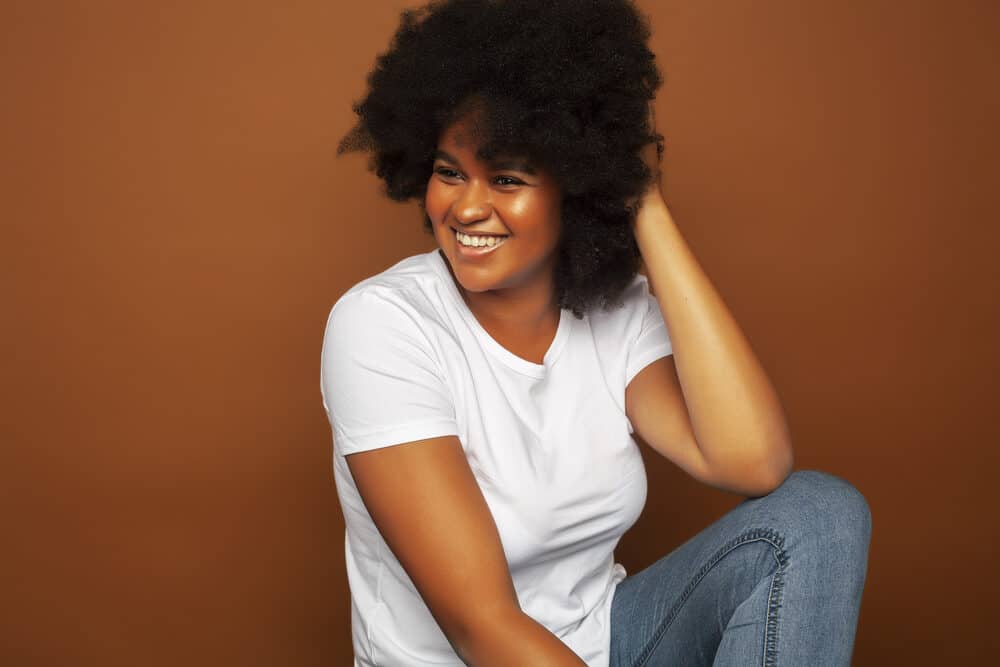 Female with kinky, coily defined curls wearing a white t-shirt and blue jeans.