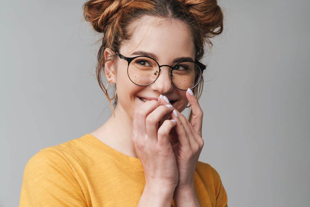 Cute white girl with type 1 natural hair and freckles wearing black glasses, gold earrings, and a yellow t-shirt.