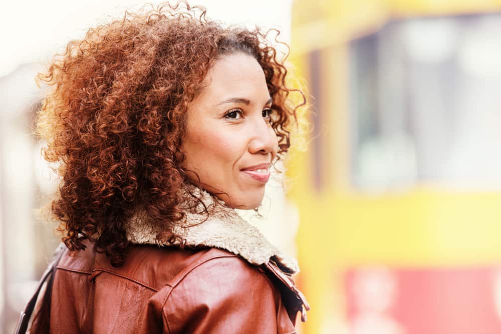  Black girl with hair valkaistu red and brown while wearing a red and brown jacket.