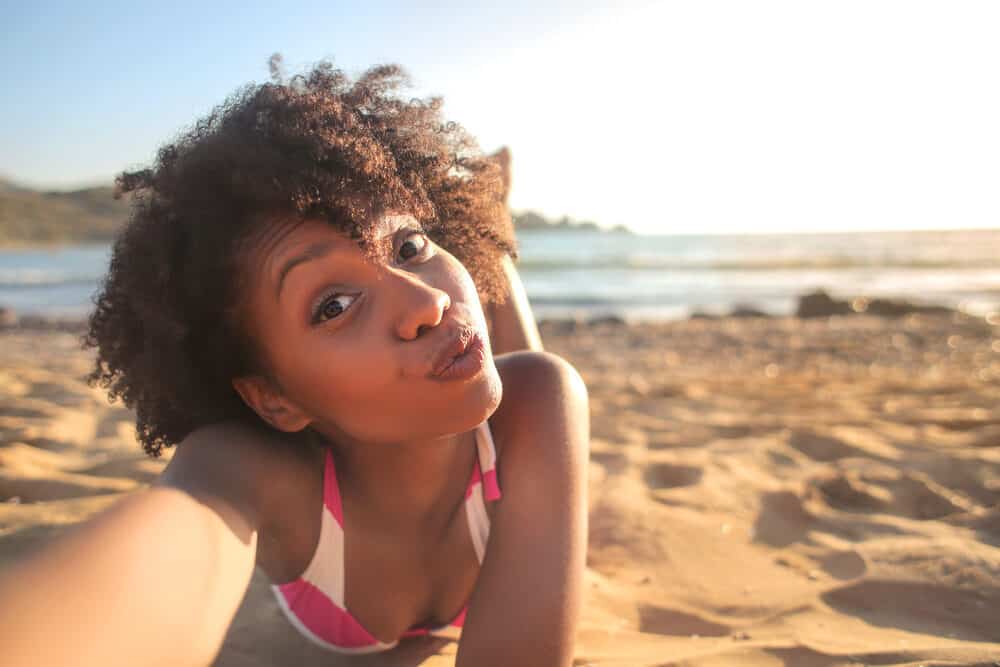 Cute black girl wearing swimwear laying on a sandy beach.