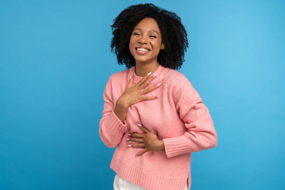 Cute female laughing while holding her chest with coily hair.