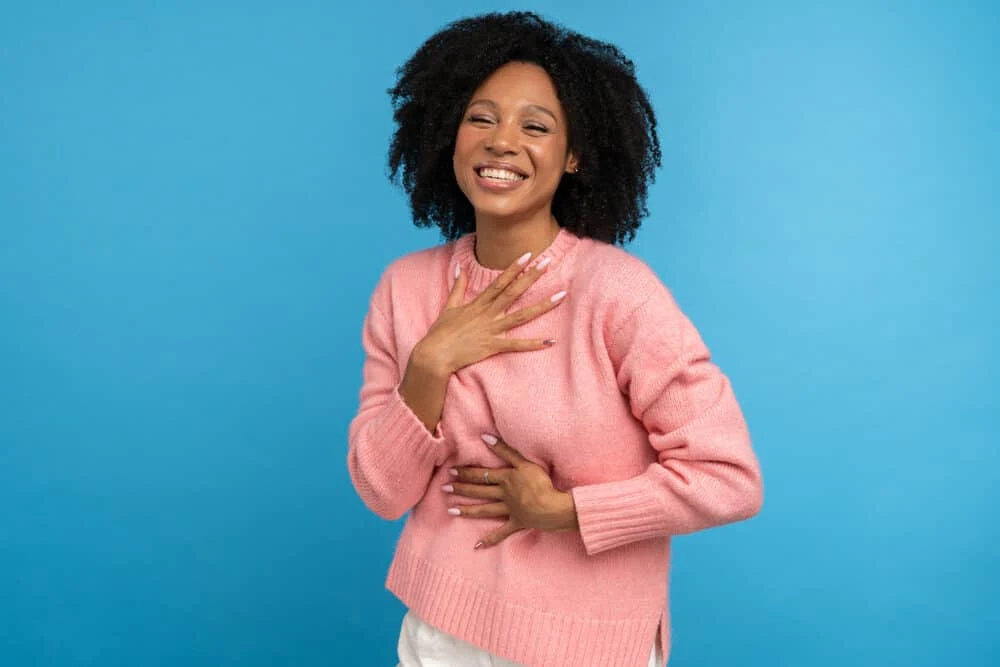 How Often Should You Moisturize Your Hair for Curls, Porosity Issues, Braids, 4C, and More 6 Cute female laughing while holding her chest with coily hair.