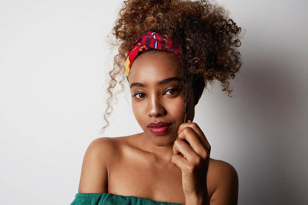 Confident young American African girl with long brown type 4a coily hair wearing an African scarf, red lipstick, and a green dress.