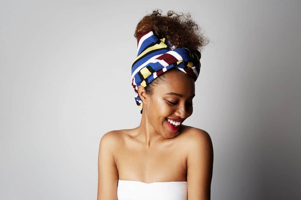 A smiling 18-year-old African girl wearing a white dress and an African scarf. She has brown, type 4a coils and is wearing red lipstick.