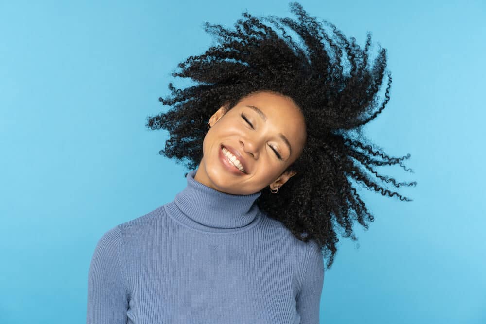 Women twirling her head as her hair rotates from one side to the other wearing a blue turtleneck shirt.