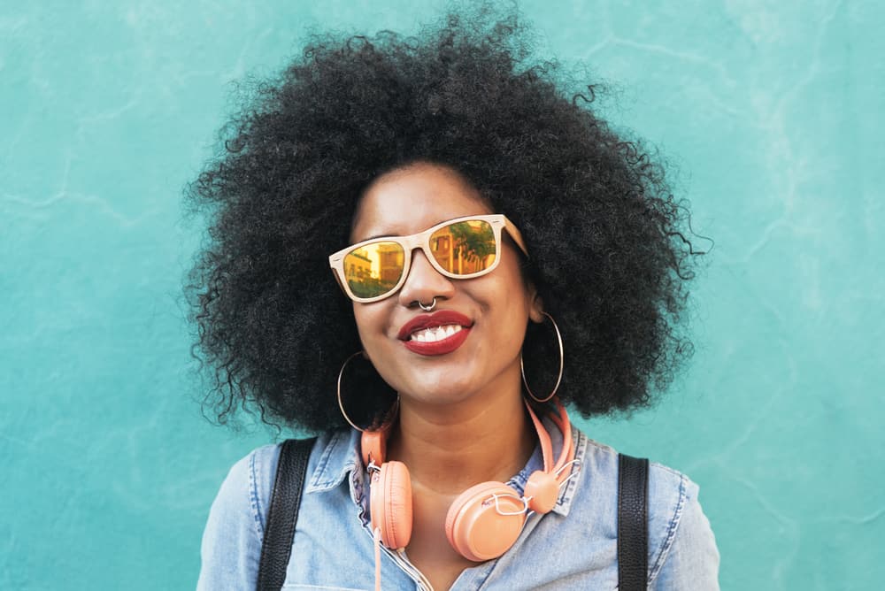 Black lady with naturally curly 4c hair strands and hoop earrings with a huge smile on her face.