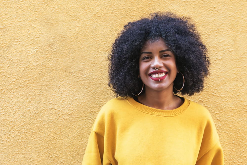 Cute black girl with a gold nose and lip ring wearing black natural hair and a yellow sweatshirt.