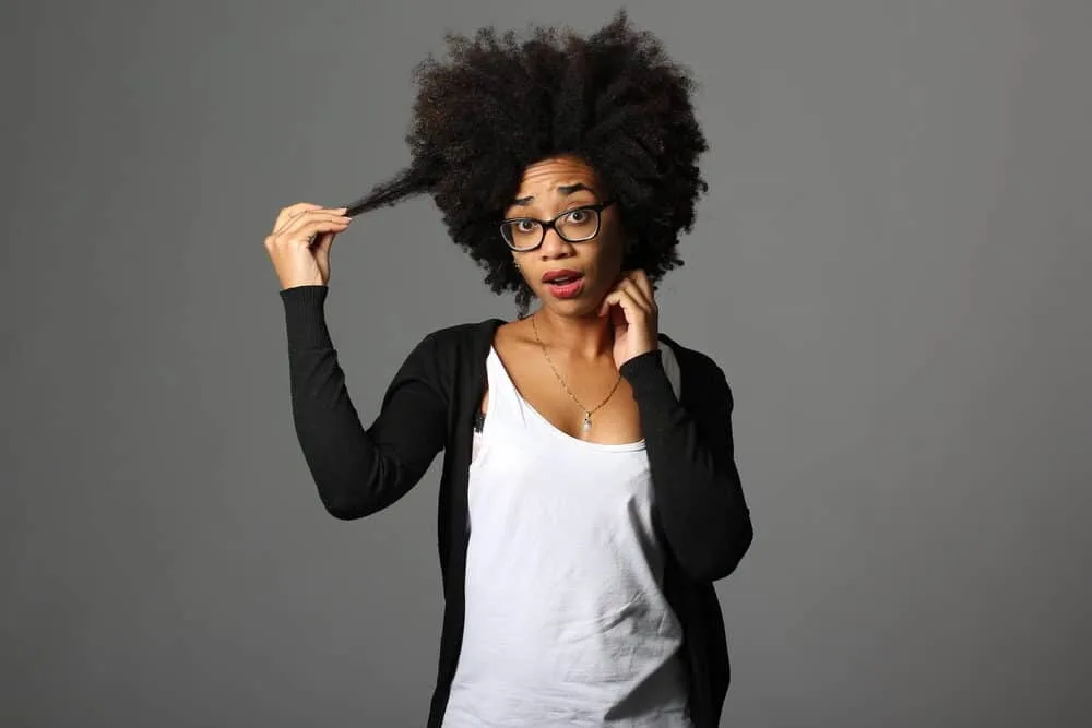 What is Coily Hair and How Do I Care for It? 13 African American lady with 4C coils wearing black pearl earrings, a silver necklace, white t-shirt, and a black knit sweater.