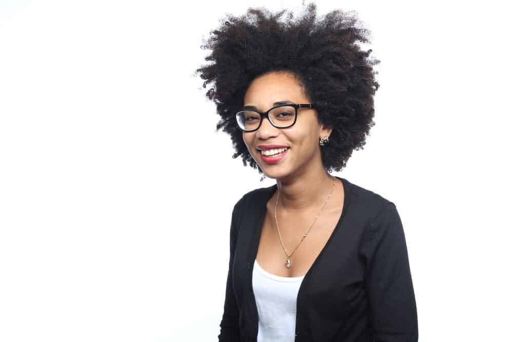 What is Coily Hair and How Do I Care for It? 9 Black girl with beautiful natural curls wearing a long silver necklace and a black sweater.
