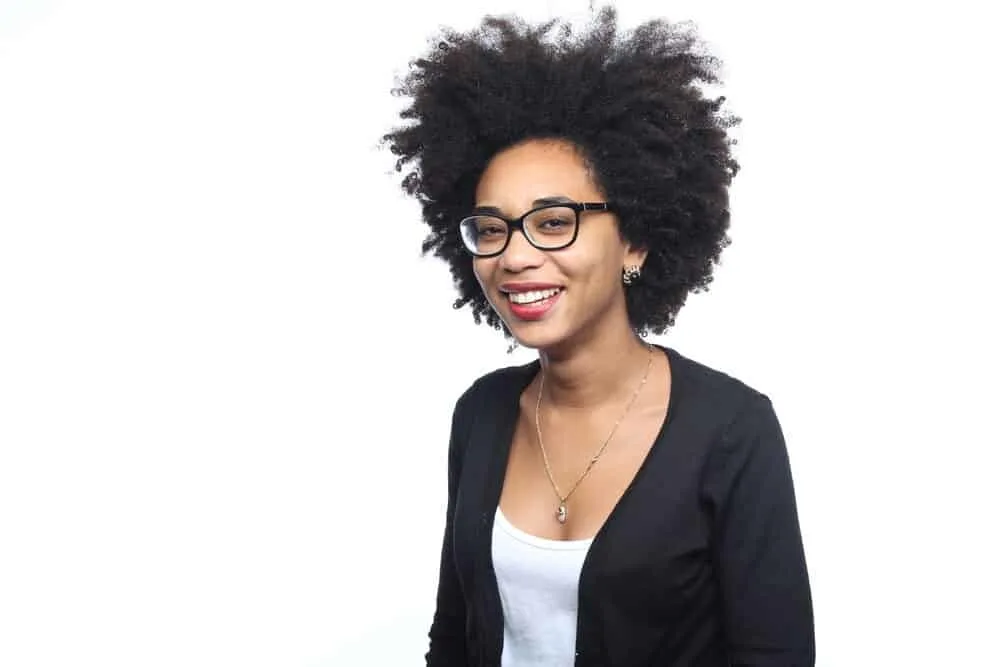 What is Coily Hair and How Do I Care for It? 9 Black girl with beautiful natural curls wearing a long silver necklace and a black sweater.